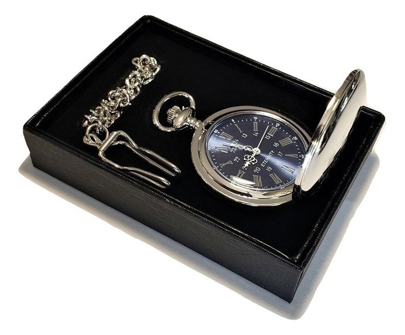 K&ouml;nnte beinhalten: Eine silberne Taschenuhr mit blauem Zifferblatt und r&ouml;mischen Ziffern. Die Uhr befindet sich in einer schwarzen Samtbox mit einer Kette und einem Taschenclip.
