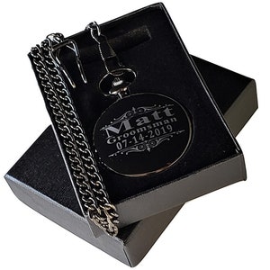 K&ouml;nnte beinhalten: Schwarze Taschenuhr mit einer silbernen Kette in einer schwarzen Box. Das Zifferblatt der Uhr ist mit dem Text "Matt Groomman 07-14-2019" graviert.