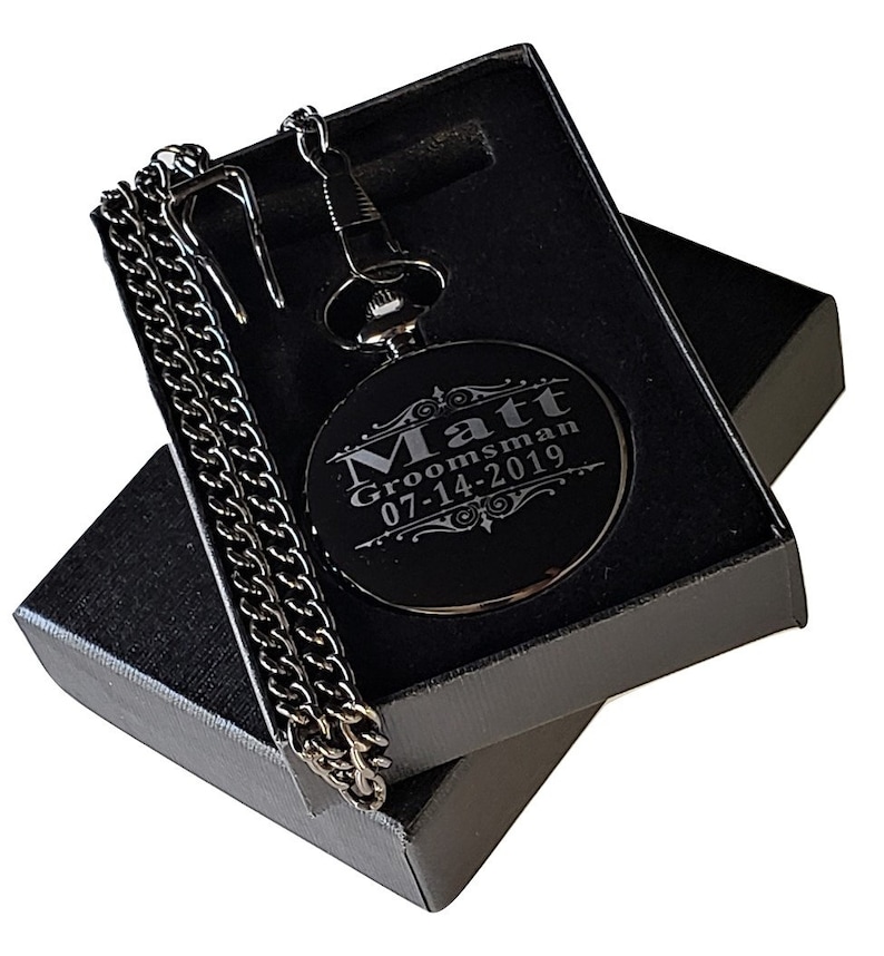 K&ouml;nnte beinhalten: Schwarze Taschenuhr mit einer silbernen Kette in einer schwarzen Box. Das Zifferblatt der Uhr ist mit dem Text "Matt Groomman 07-14-2019" graviert.