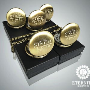 May include: Five gold pocket watches with engraved names and dates on black velvet boxes. The watches have a chain attached to them. The boxes are arranged in a row on a gray background. The text on the watches reads "Tucarella Groomsman 5.26.18", "Long Groomsman 5.26.18", "Rizzo Officiant 26.18", "Singh Groomsman 5.26.18", and "Minichino Jr. Groomsman 5.26.18".