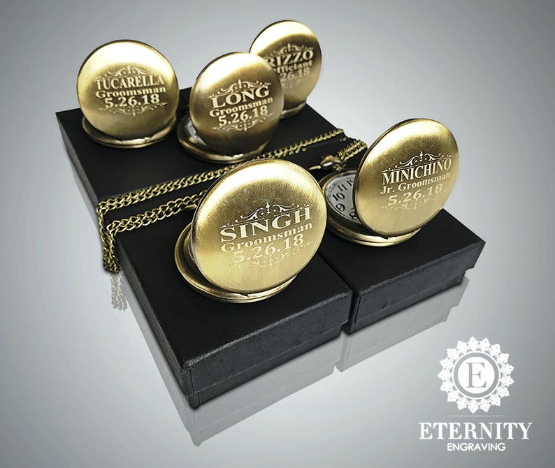 May include: Five gold pocket watches with engraved names and dates on black velvet boxes. The watches have a chain attached to them. The boxes are arranged in a row on a gray background. The text on the watches reads "Tucarella Groomsman 5.26.18", "Long Groomsman 5.26.18", "Rizzo Officiant 26.18", "Singh Groomsman 5.26.18", and "Minichino Jr. Groomsman 5.26.18".