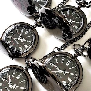 May include: Four black pocket watches with chains. Each watch has a black face with Roman numeral hour markers and a red inscription that reads "ETERNITY".