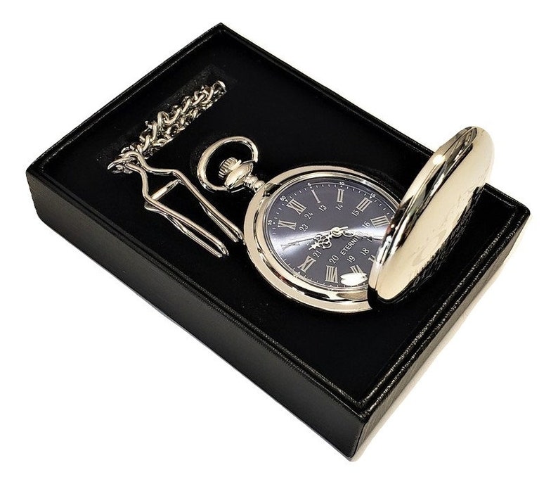 K&ouml;nnte beinhalten: Eine silberne Taschenuhr mit schwarzem Zifferblatt und r&ouml;mischen Ziffern f&uuml;r die Stunden. Die Uhr befindet sich in einer schwarzen Samtbox mit einer Kette.