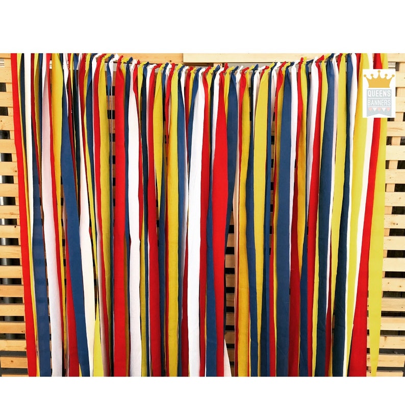 Puede incluir: Un tel&oacute;n de fondo colorido con tiras de tela verticales en rojo, amarillo, blanco y azul marino. Las tiras cuelgan de una estructura de madera, creando una exhibici&oacute;n vibrante y texturizada. El logotipo "QUEENS BANNERS" es visible en la esquina superior derecha.