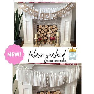 Op de afbeelding: Een banner van jute met de tekst "Baby in Bloom" hangt boven een witte open haard. Een witte stoffen slinger met witte pompoenen hangt onder de open haard. De tekst "fabric garland sold separate" staat onder de afbeelding.