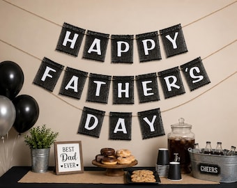 Puede incluir: Una pancarta negra con letras blancas que forman HAPPY FATHER'S DAY cuelga sobre una mesa con donas, un dispensador de bebidas, un letrero que dice BEST DAD EVER y un cubo de metal con la etiqueta CHEERS, junto a globos negros y plateados.