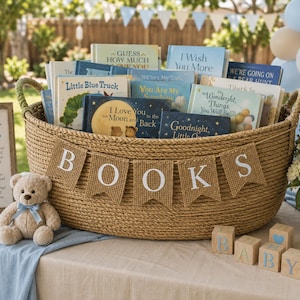 Op de afbeelding: Een grote, ronde, gevlochten beige mand gevuld met diverse kinderboeken, voorzien van een jute banner met de witte letters B-O-O-K-S. Naast de mand staat een lichtbruine teddybeer met een blauw lint en houten blokken met de tekst BABY.
