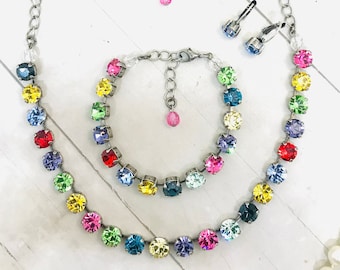 May include: A rainbow crystal necklace, bracelet and earrings set. The necklace and bracelet feature a silver chain with colourful round crystals. The earrings are silver hoops with a blue crystal.