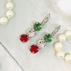 May include: A pair of silver dangle earrings with red, white, and green crystal stones. The earrings have a hook closure.