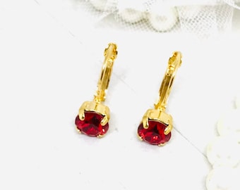 May include: A pair of gold hoop earrings with a red gemstone dangling from each hoop.