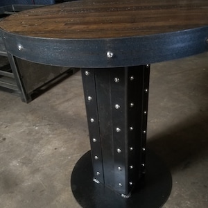 May include: A round wooden table top with a black metal rim and base. The base is made of metal and has a series of rivets around the edge.