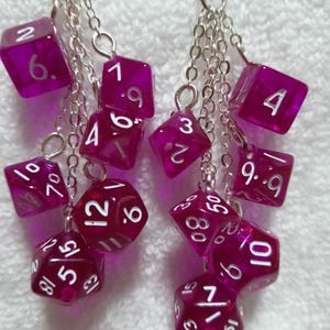 May include: Earrings with multiple translucent purple dice with white numerals, suspended by silver chains. The dice are various shapes, including six-sided and multi-sided. A fun accessory for tabletop gaming enthusiasts.