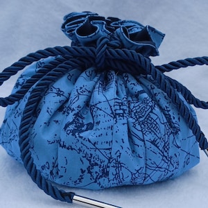 Könnte beinhalten: Ein blauer Beutel mit Kordelzug und Kartenmuster. Der Beutel ist aus Stoff gefertigt und hat einen dunkelblauen Kordelverschluss. Der Beutel hat einen Durchmesser von etwa 15 cm.