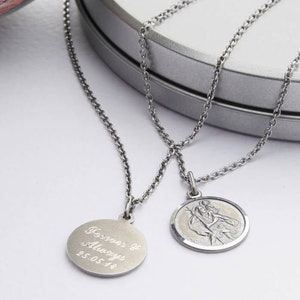 Op de afbeelding: Twee zilveren kettingen met hangers. Een hanger is een ronde schijf met de inscriptie "Forever & Always 25.05.14". De andere hanger is een ronde schijf met een religieus beeld.