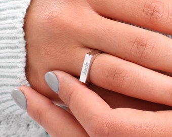 May include: A silver ring with a rectangular band engraved with the name "Jack".
