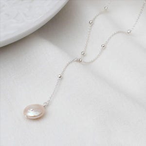 May include: A silver chain necklace with small silver beads and a large, off-white pearl pendant.