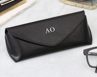 May include: Black leather glasses case with a flap closure and the initials "AO" embossed in white on the front.