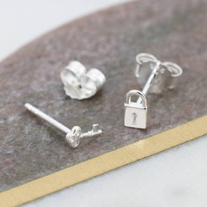 May include: A pair of silver earrings, one shaped like a key and the other like a padlock. The key has three small stones on the head.