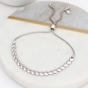 May include: A silver adjustable bracelet with a chain and a row of heart-shaped charms.