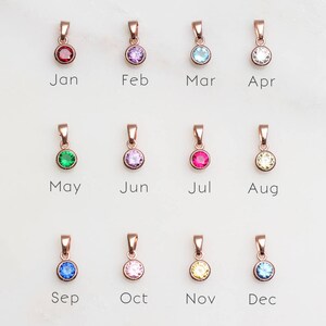 May include: Twelve rose gold pendants with different colored gemstones, each representing a month of the year. January is red, February is purple, March is blue, April is white, May is green, June is light purple, July is red, August is yellow, September is blue, October is pink, November is yellow, and December is blue.