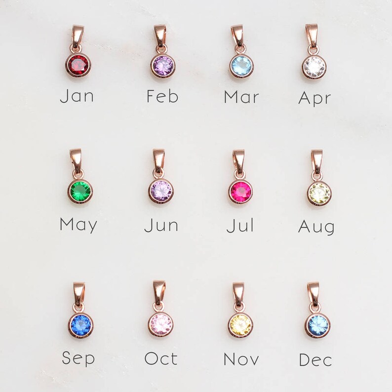 May include: Twelve rose gold pendants with different colored gemstones, each representing a month of the year. January is red, February is purple, March is blue, April is white, May is green, June is light purple, July is red, August is yellow, September is blue, October is pink, November is yellow, and December is blue.