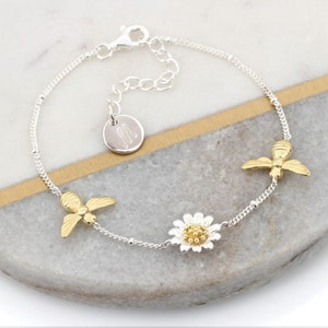 May include: Silver chain bracelet with a gold daisy charm, two gold bee charms, and a silver charm with the letter "M" engraved on it.
