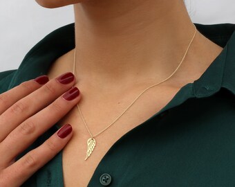 May include: A gold chain necklace with a delicate angel wing pendant. The necklace is worn by a person with red nail polish.