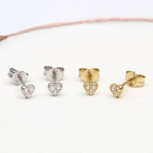 Puede incluir: Tres pares de pequeños pendientes en forma de corazón con pequeñas piedras transparentes. Los pendientes son de plata, oro y oro rosa.