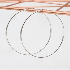 May include: A pair of silver hoop earrings. The hoops are large and circular, and they are made of a thin metal.