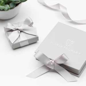 May include: Two grey gift boxes with white satin ribbon bows. The larger box has the text "HURLEYEURLEY" printed on the top.