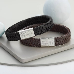 Può includere: Due braccialetti in pelle intrecciata con chiusure in metallo argentato. La chiusura del braccialetto nero ha il testo "Your one & only" e un design ad ala. La chiusura del braccialetto marrone ha il testo "Love & Protection" e un design ad ala.