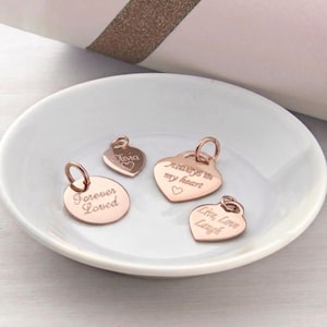 Peut inclure: Quatre breloques en métal doré rose avec anneaux de jonction. Une breloque ronde est gravée Forever Loved. Un petit cœur porte l'inscription Olivia avec un cœur. Un grand cœur porte Always in my heart avec un cœur. Un cœur porte Live, Love Laugh.