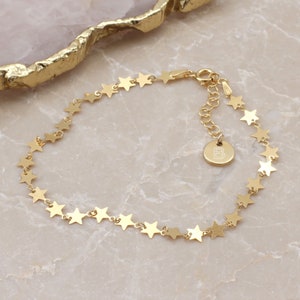 May include: Gold star charm bracelet with a small round charm engraved with the letter "B".