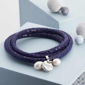 May include: A navy blue leather bracelet with a silver charm that says "Rebecca" and two white pearl accents.