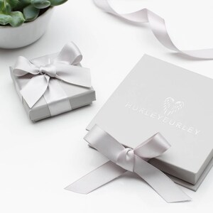 May include: Two gray gift boxes with white satin ribbon bows. The larger box has the text "HURLEYEURLEY" printed on the top.