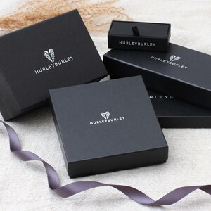 May include: Three black boxes with the Hurley Burley logo. The boxes are stacked on top of each other. The top box is smaller than the other two boxes.