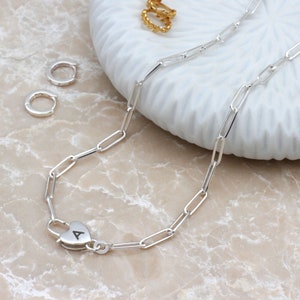 May include: A silver chain necklace with a heart-shaped pendant. The pendant has the letter "A" engraved on it.