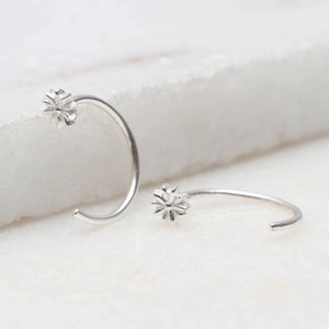 May include: A pair of silver hoop earrings with a small flower design on each hoop.