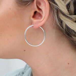 Peut inclure: Boucles d'oreilles créoles en argent. Les boucles d'oreilles sont simples et classiques, avec une finition lisse et polie.