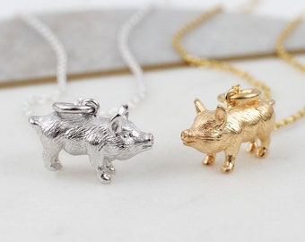 May include: Two necklaces featuring three-dimensional pig charms, one in a polished silver tone and one in a gold tone. Each pendant is suspended from a matching delicate metal chain, showcasing detailed textures on the pig's body and ears.