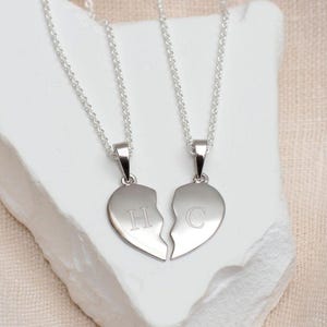 Peut inclure: Deux colliers en argent avec des pendentifs en forme de cœur brisé assortis. Les pendentifs sont gravés des lettres "H" et "C".
