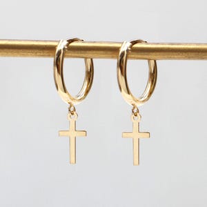 May include: Gold hoop earrings with a dangling cross charm. The earrings are simple and elegant.