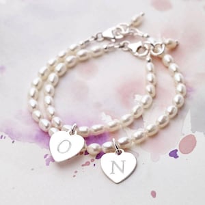 Op de afbeelding: Twee delicate parel armbanden met zilveren hartcharms gegraveerd met de letters "O" en "N".