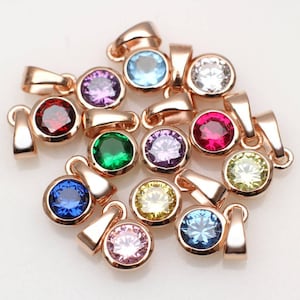 May include: Assortment of 12 rose gold pendants with round colorful gemstones. Each pendant features a loop for attaching to a chain or cord.
