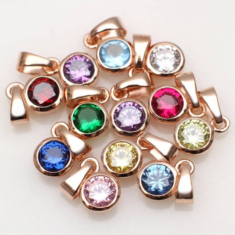May include: Assortment of 12 rose gold pendants with round colorful gemstones. Each pendant features a loop for attaching to a chain or cord.