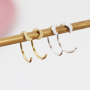 May include: Two pairs of crescent moon hoop earrings. One pair is gold and the other is silver.