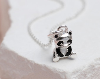 Könnte beinhalten: Eine silberne Halskette mit einem kleinen Panda-Anhänger. Der Panda ist schwarz und weiß mit einer silbernen Umrandung.