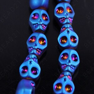 May include: A strand of blue, purple, and orange skull beads. The beads are made of hematite and have a shiny, metallic finish.