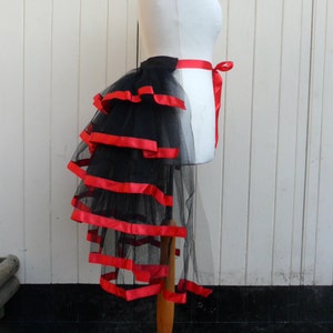 May include: A black tulle bustle with red satin ribbon trim. The bustle is layered and has a long train.