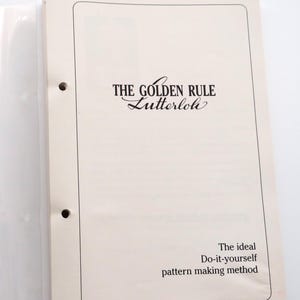 May include: An open binder with a clear plastic cover and a cream-colored page. The page features the title "THE GOLDEN RULE Lutterloh" in black script. Below the title is the text "The ideal Do-it-yourself pattern making method."